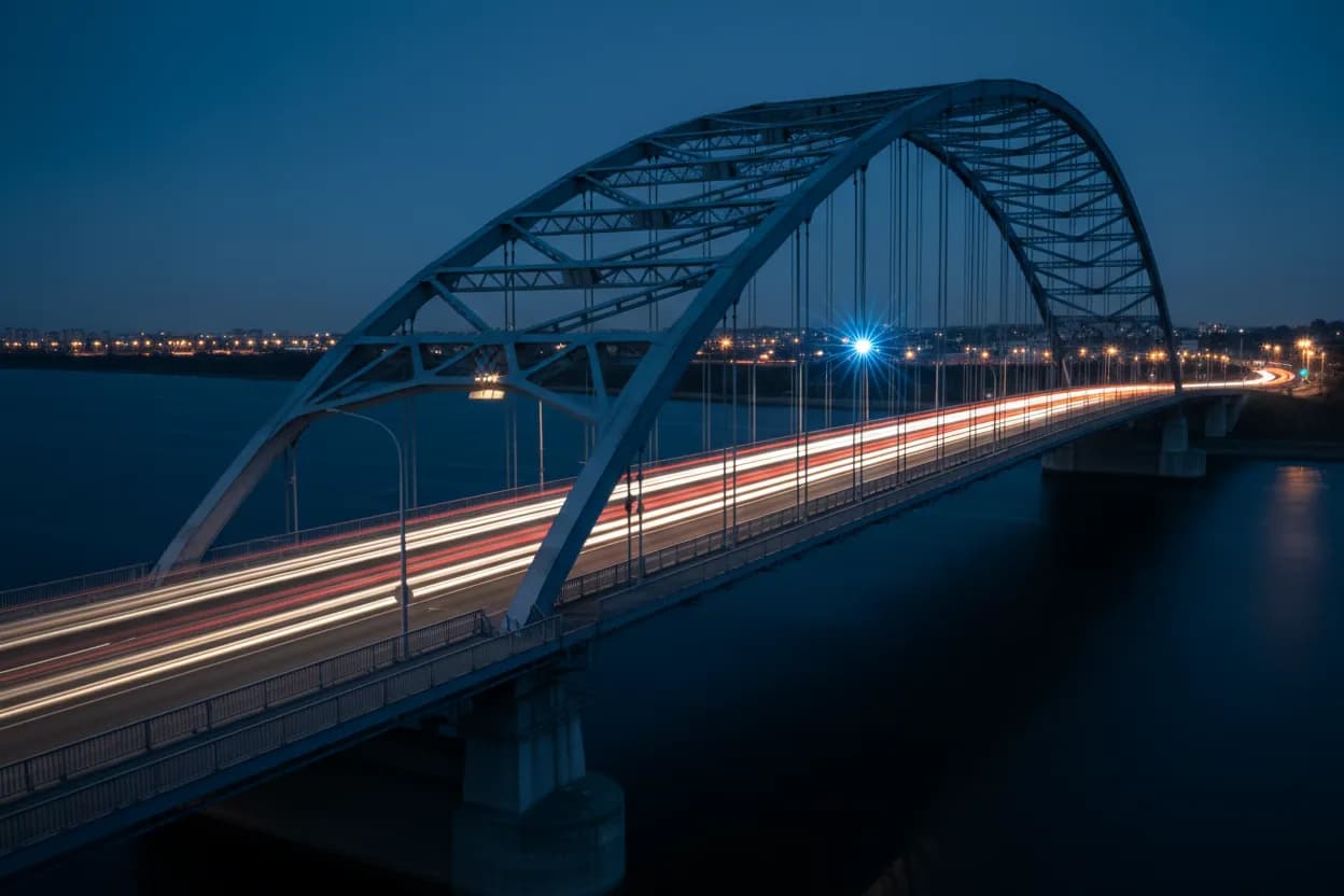 Steel arch bridge with light trails at blue hour